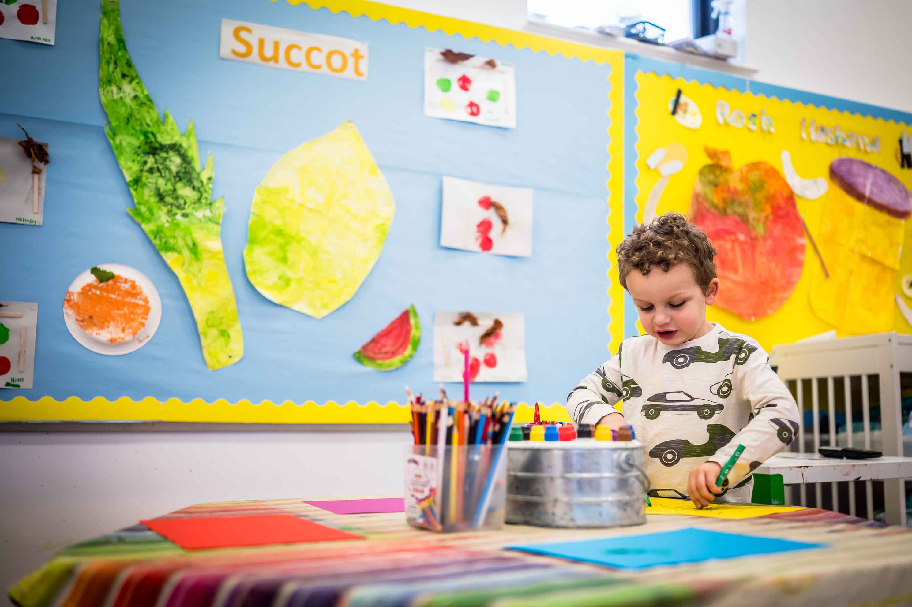 Jewish boy at a werton nursery playing with colouring, with jewish education materials in the backdrop